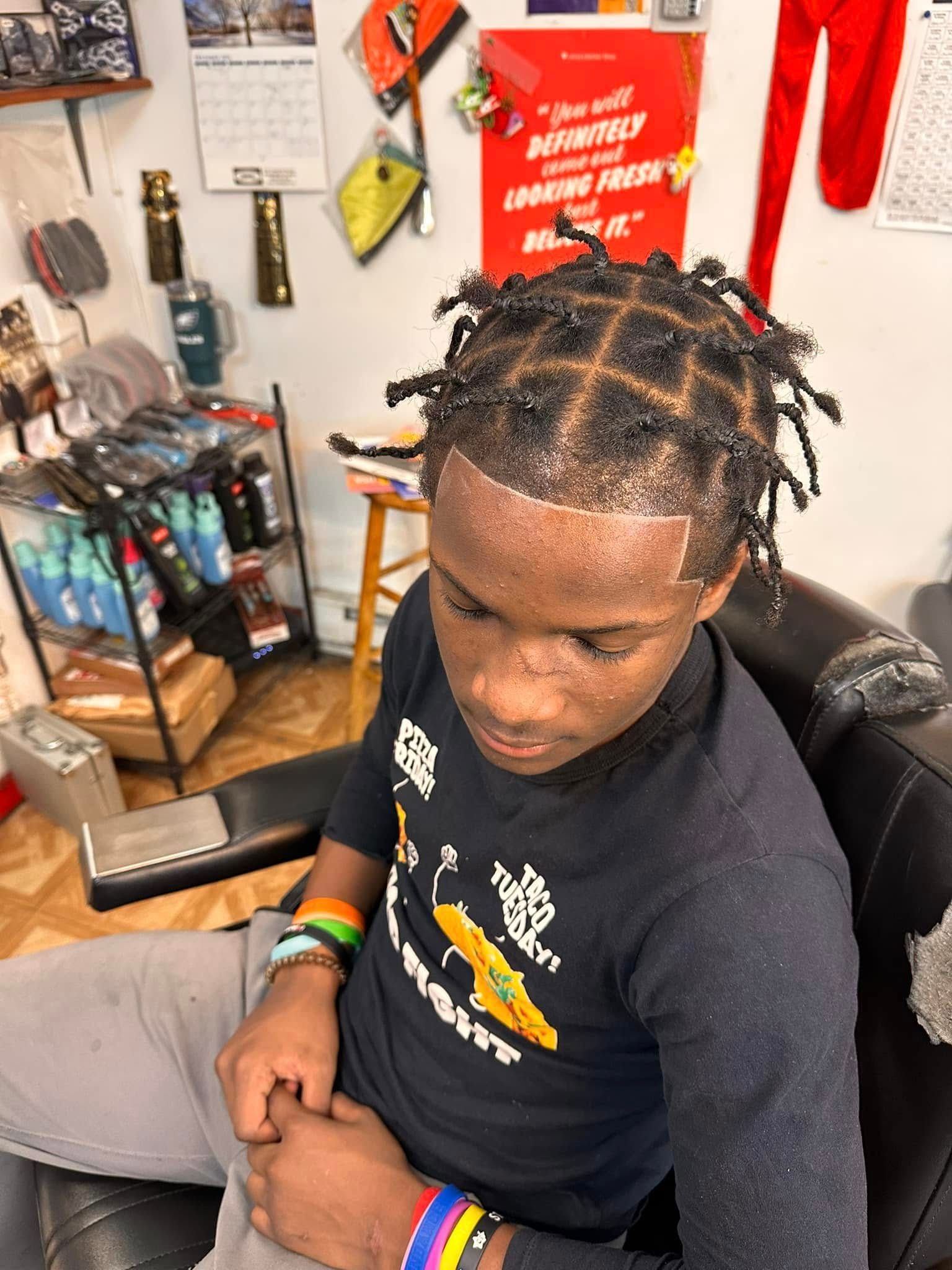 A person in a barber chair with a fresh taper fade haircut and box braids styled into a grid pattern.