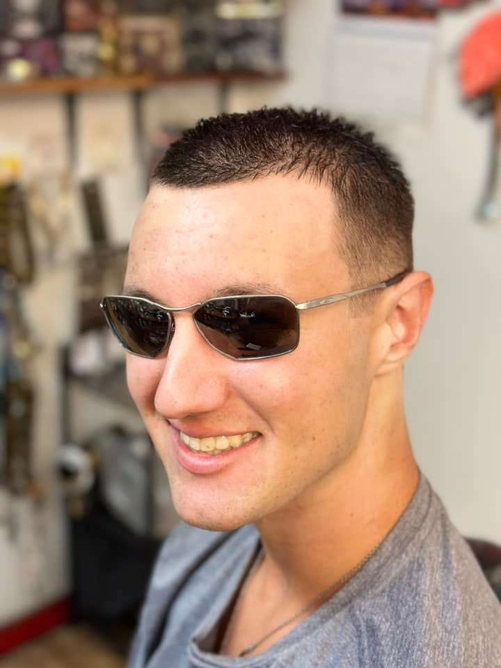 A smiling person wearing silver-framed sunglasses and a grey t-shirt in a retail shop.