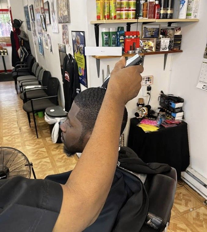 A barber uses electric clippers to trim the hair of a client sitting in a salon chair.