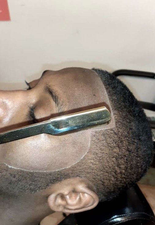 A barber’s straight razor held against the temple of a person’s head to create a sharp hairline edge.