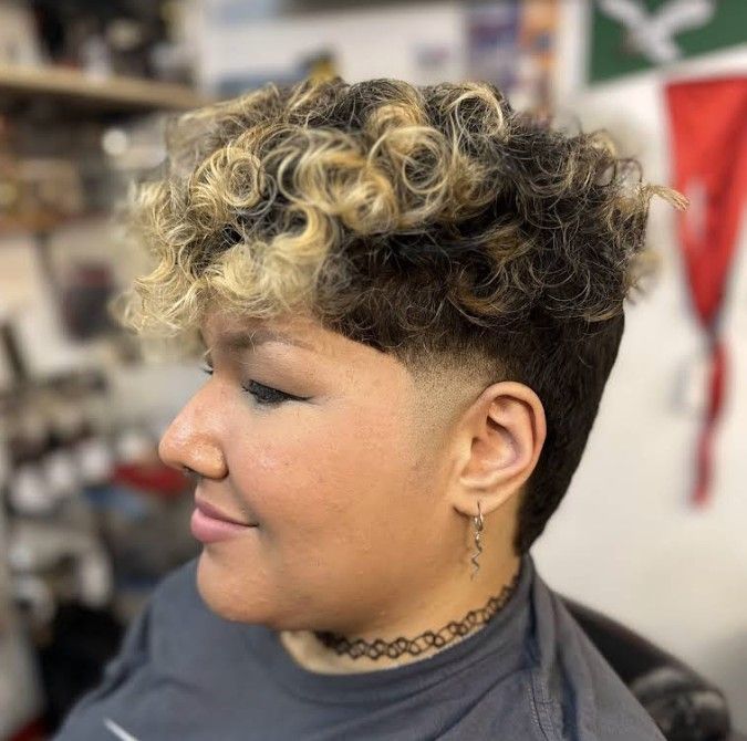 A profile view of a person with a short, curly, two-toned blonde and brown hairstyle featuring a faded side undercut.
