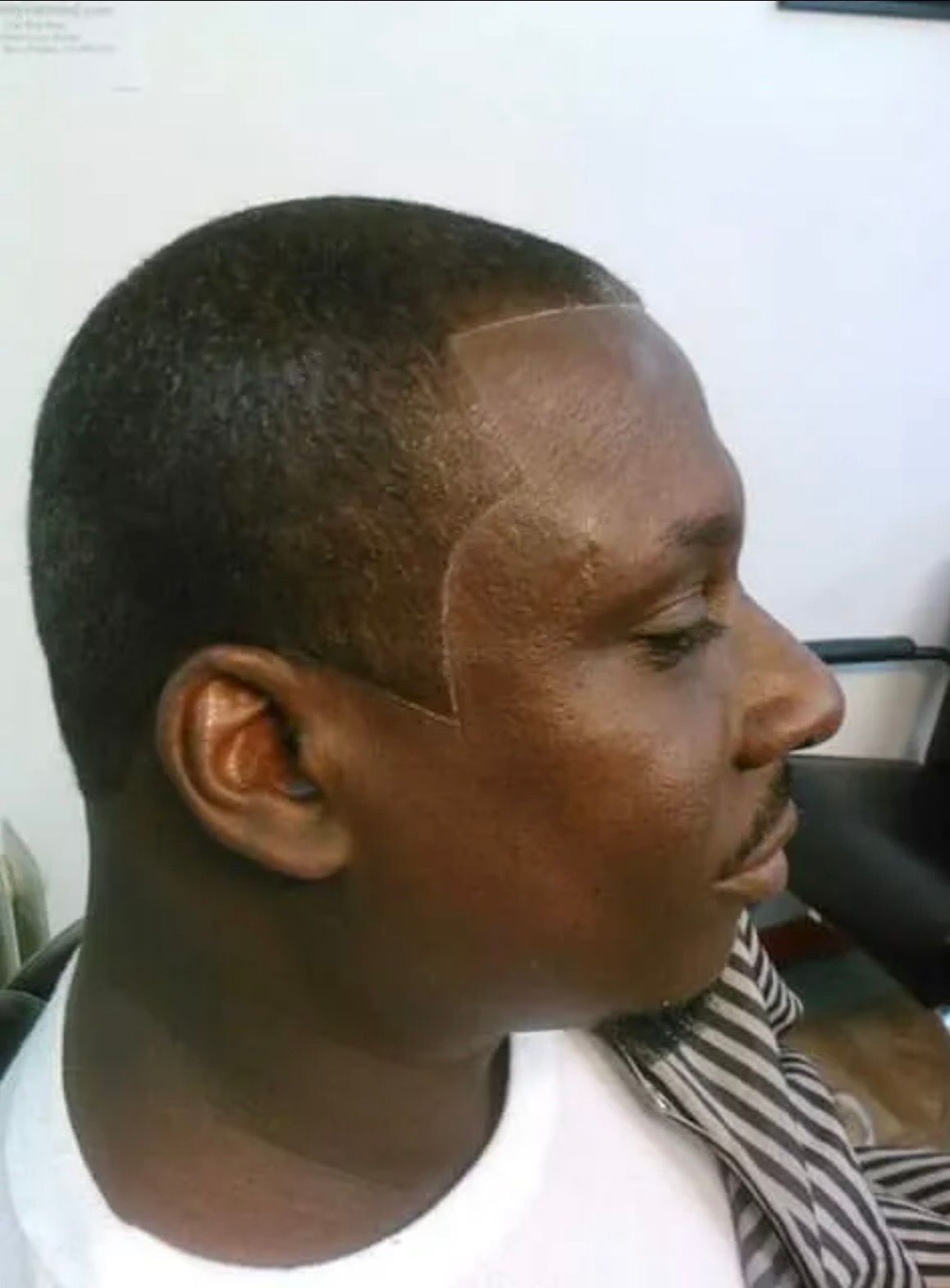 A side-view close-up of a person with a short, precision-cut fade and a sharply defined, curved hairline design.