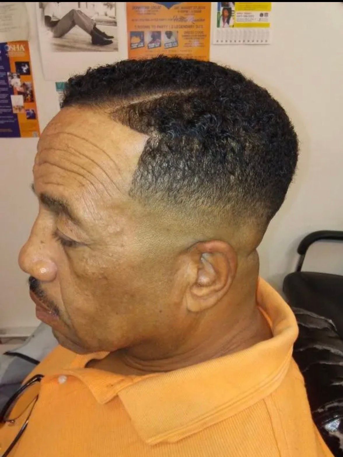 A side-profile view of a man with a short, faded haircut featuring a sharp, clean temple line-up and a part.