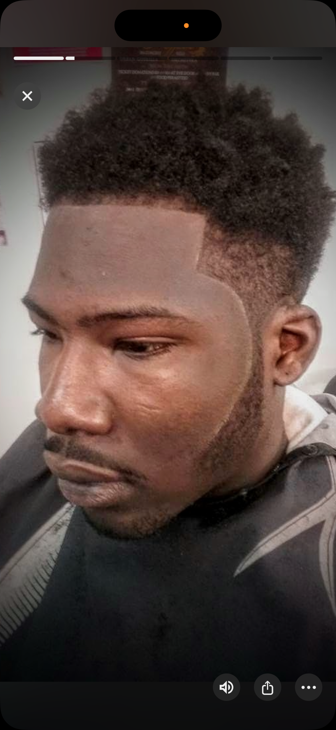 A close-up view of a person with a fresh, sharp haircut and a neatly lined-up beard, seated in a barbershop.
