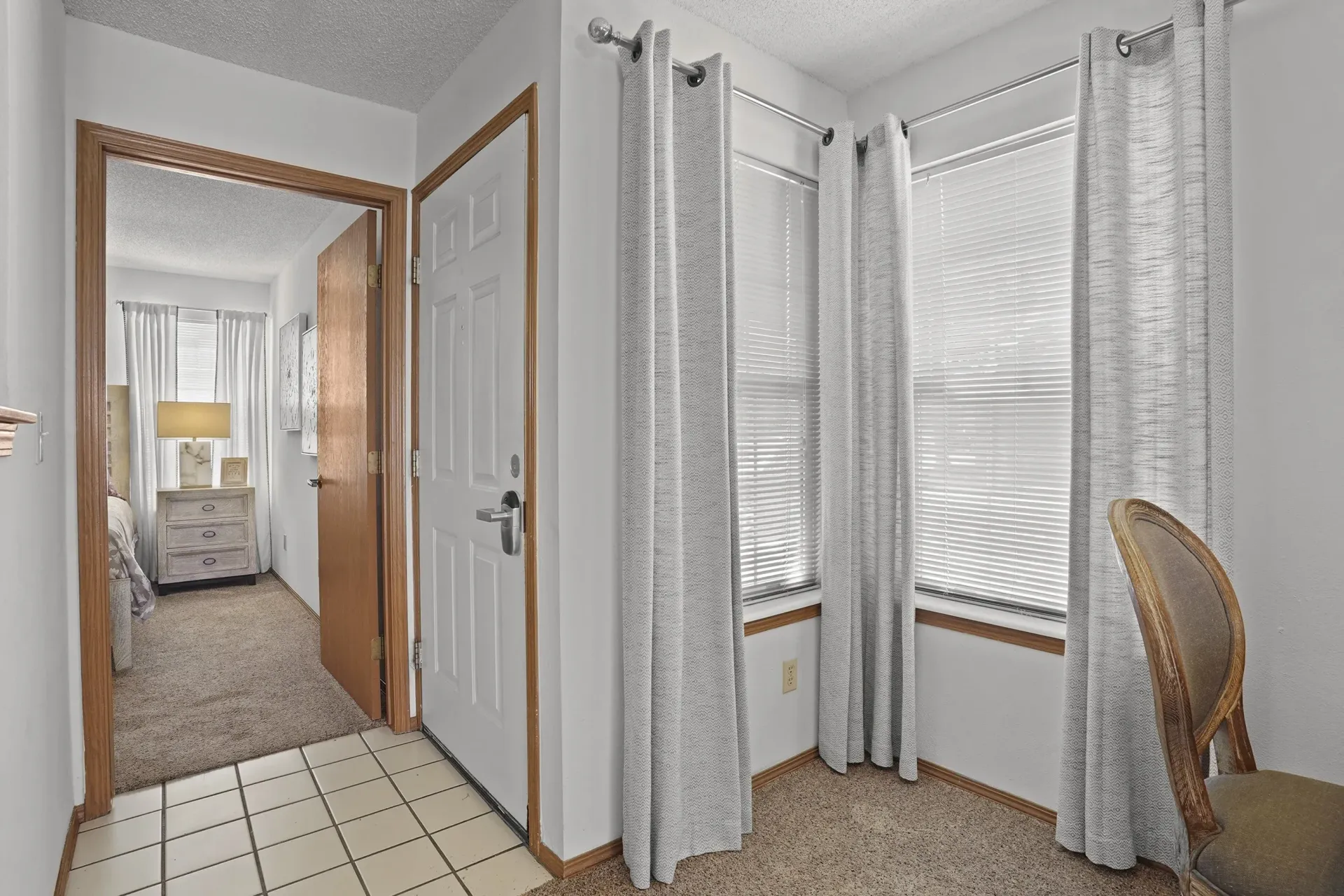 A room with a chair and a bed in the background.