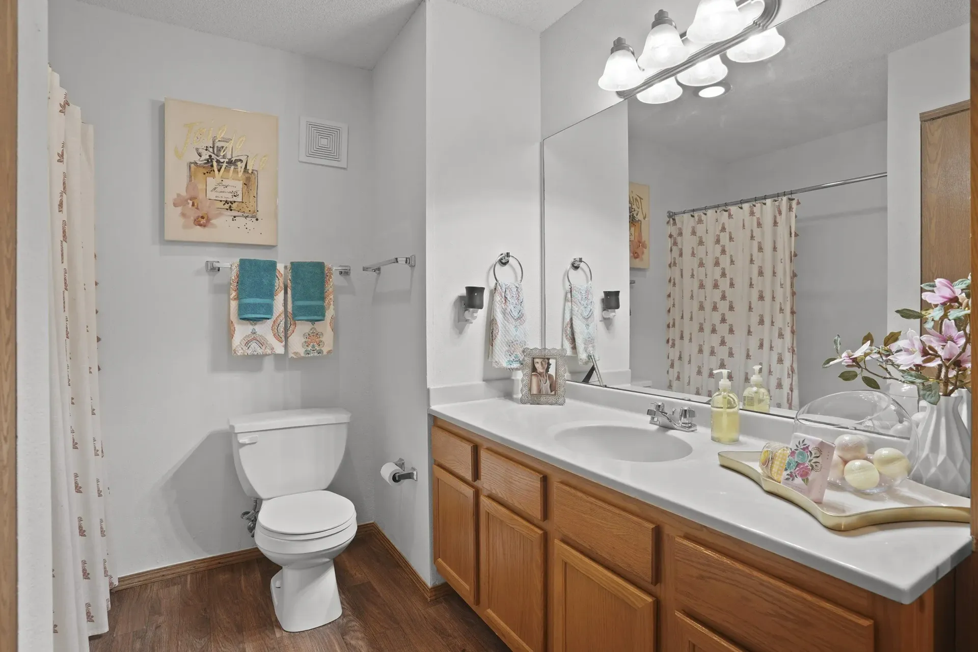 A bathroom with a toilet, sink, mirror, and a painting on the wall.