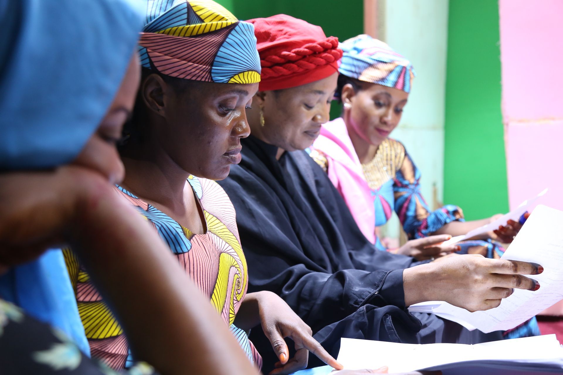 Women in colorful headscarves and dresses review papers indoors, focused on their work.
