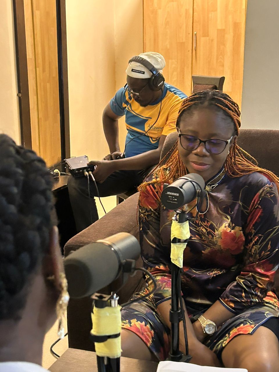 Woman with microphone, recording podcast, with a crew in the background operating equipment.