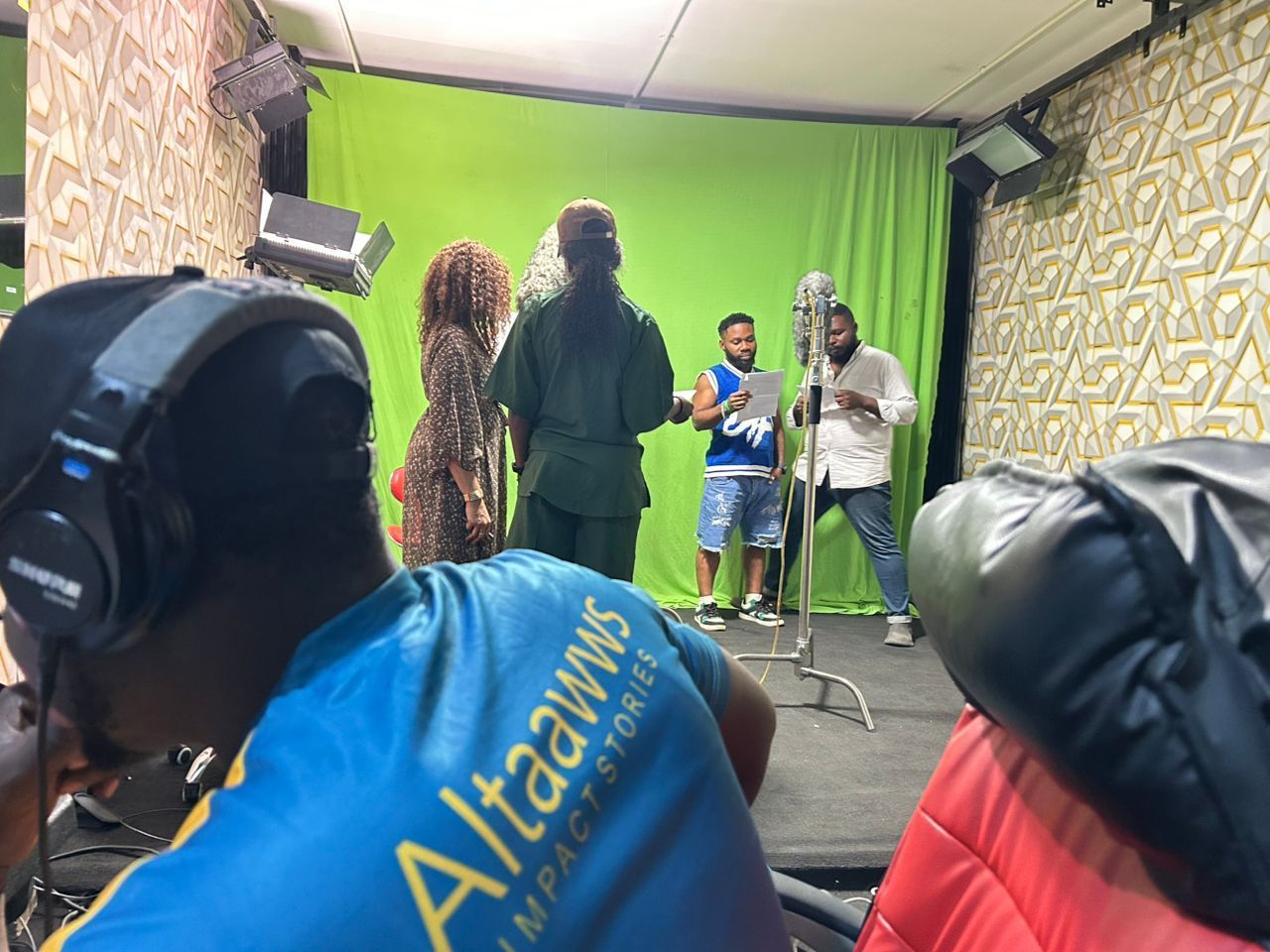 Film crew in a studio. Actors on a green screen stage, crew member with headphones.
