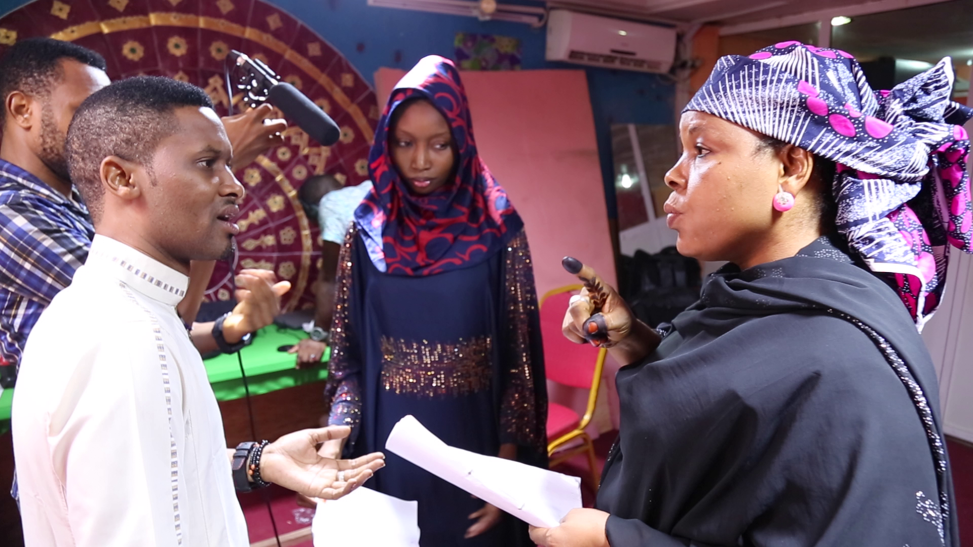 People filming inside, woman pointing, others looking on.