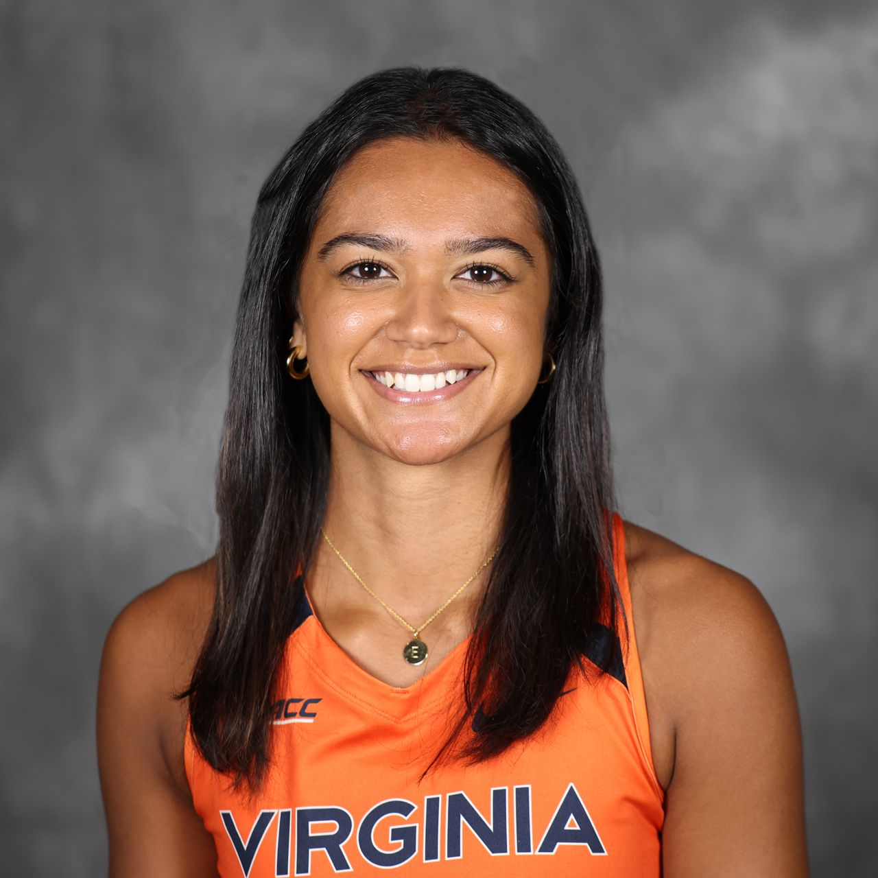 Smiling athlete in navy and orange sportswear, arms crossed against a plain light background