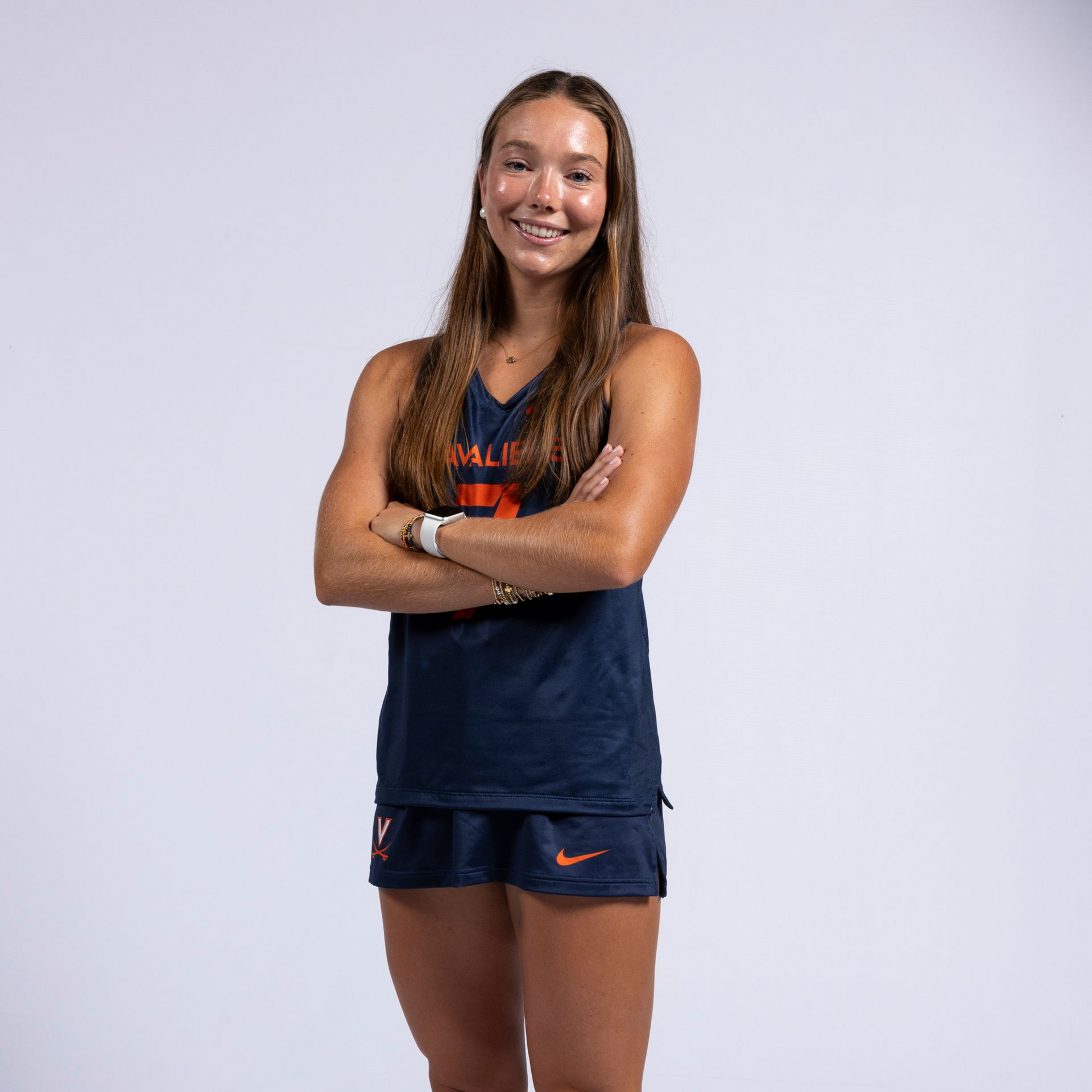 Smiling athlete in navy and orange sportswear, arms crossed against a plain light background