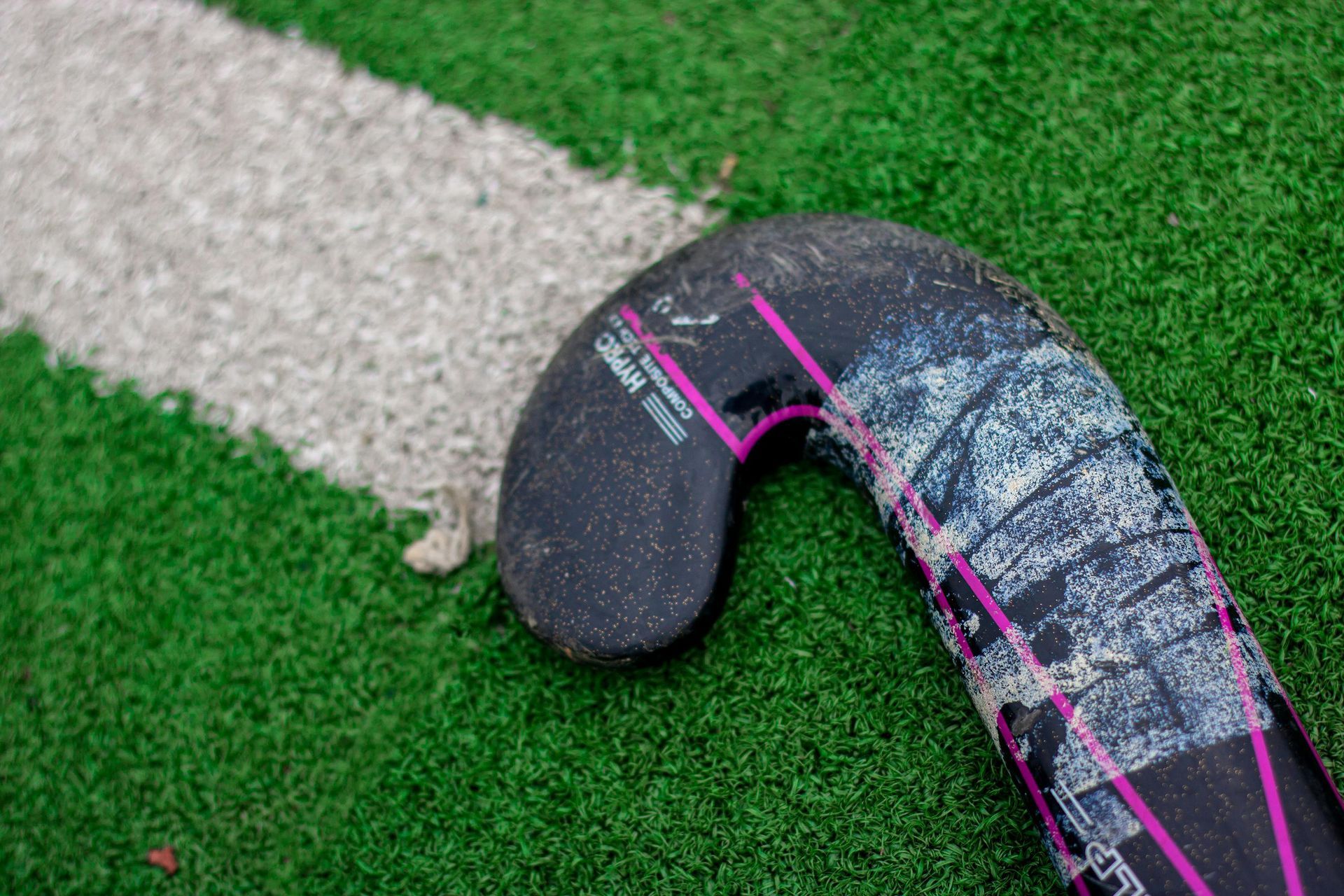 Hockey stick blade on green turf beside a white boundary line