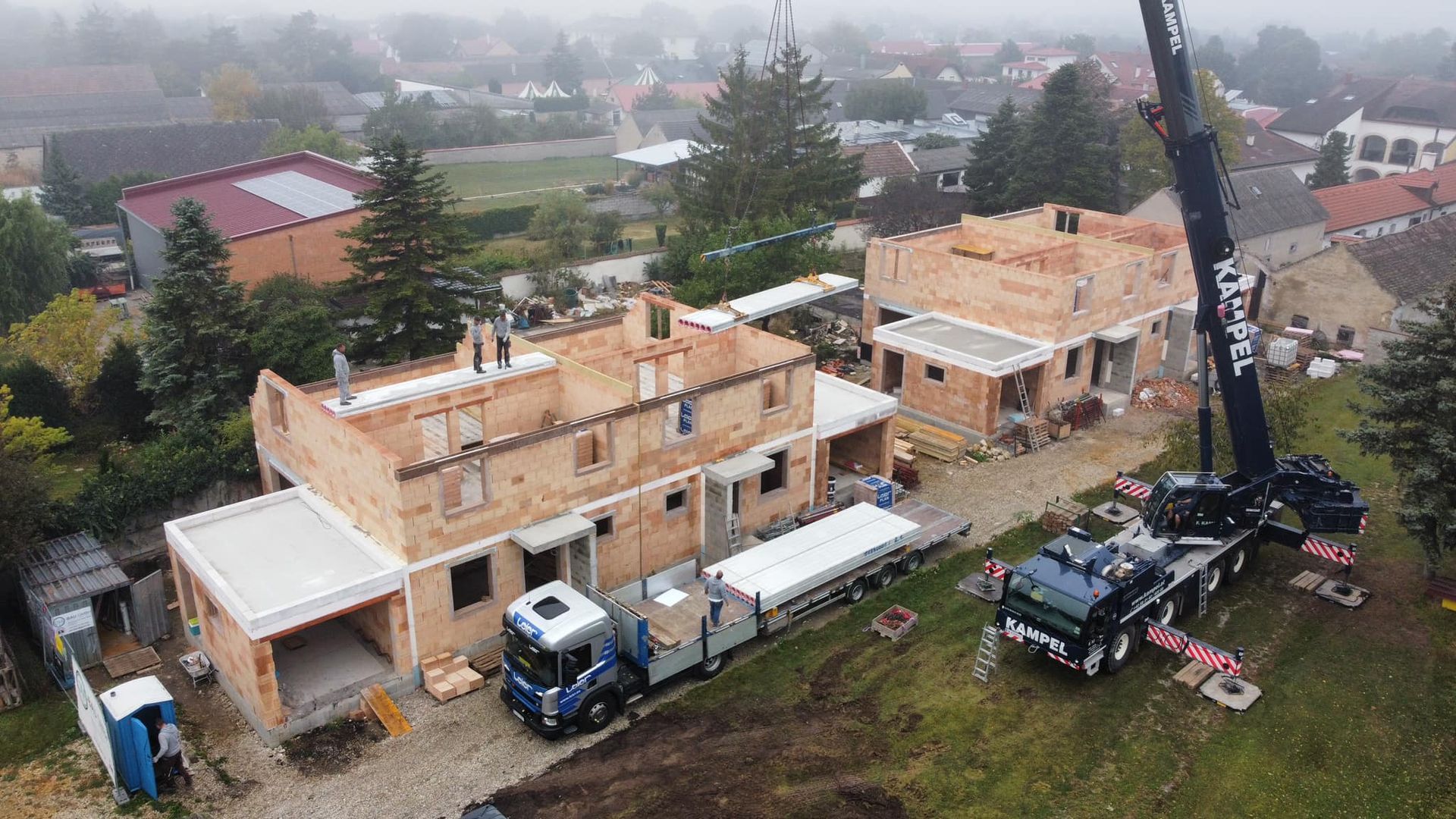Zwei Bauarbeiter in Westen und Schutzhelmen besichtigen eine Baustelle, ein Kran ist zu sehen.