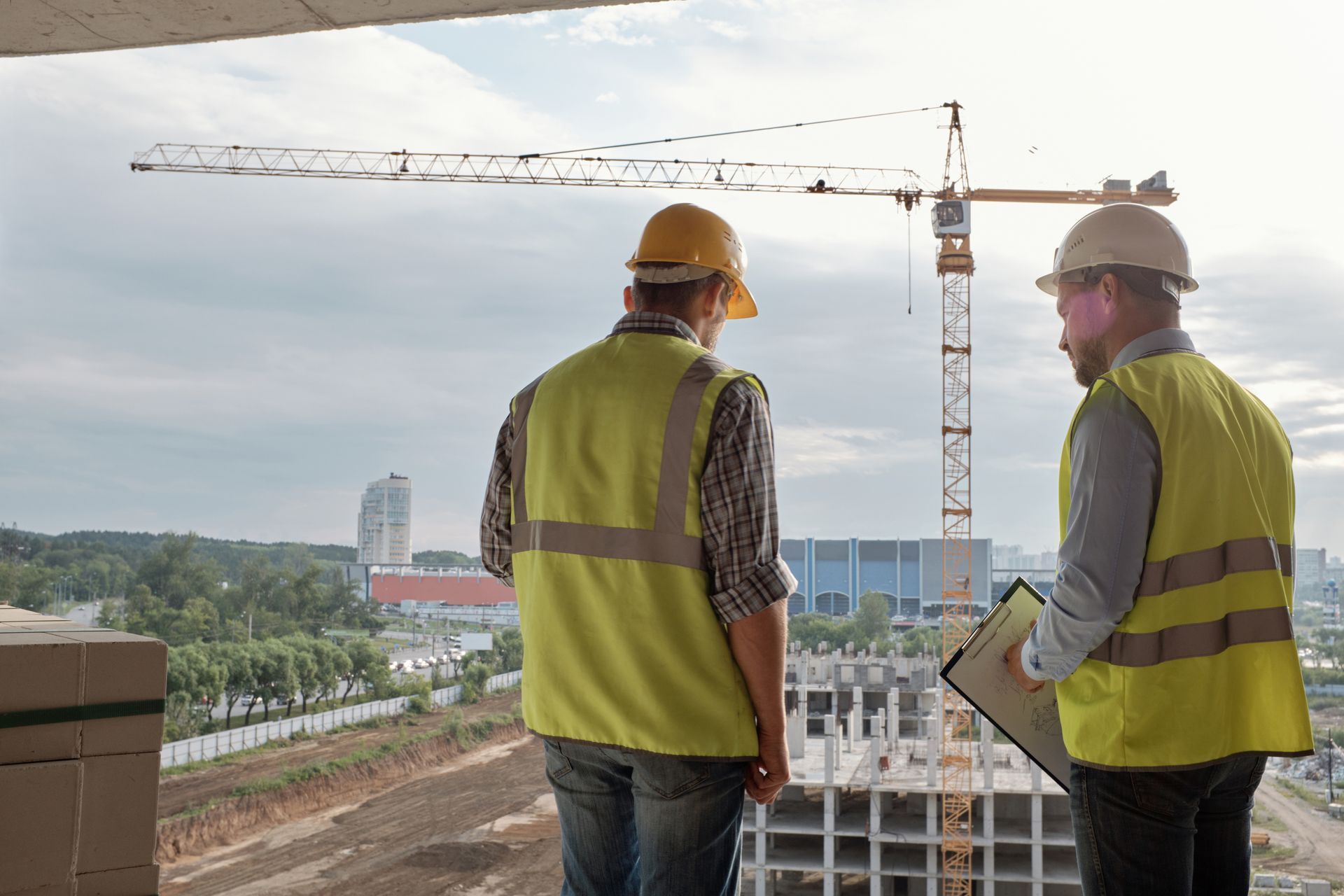 Zwei Bauarbeiter in Westen und Schutzhelmen besichtigen eine Baustelle, ein Kran ist zu sehen.