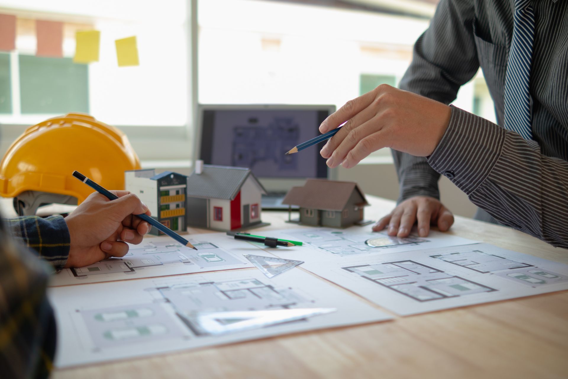 Zwei Personen arbeiten gemeinsam an Architekturplänen, kleine Hausmodelle auf dem Schreibtisch.