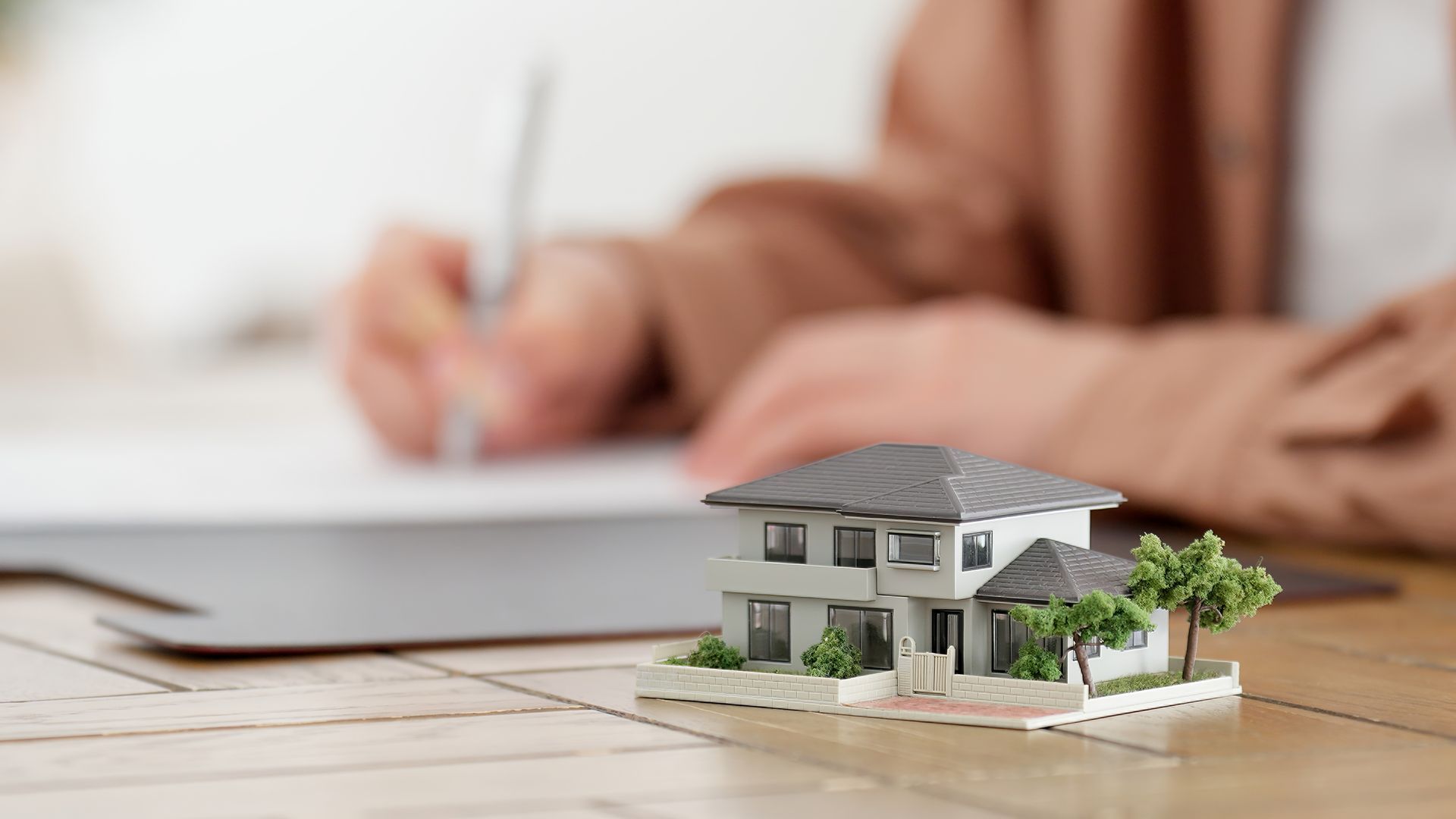 Miniaturhausmodell mit einer schreibenden Person im Hintergrund.
