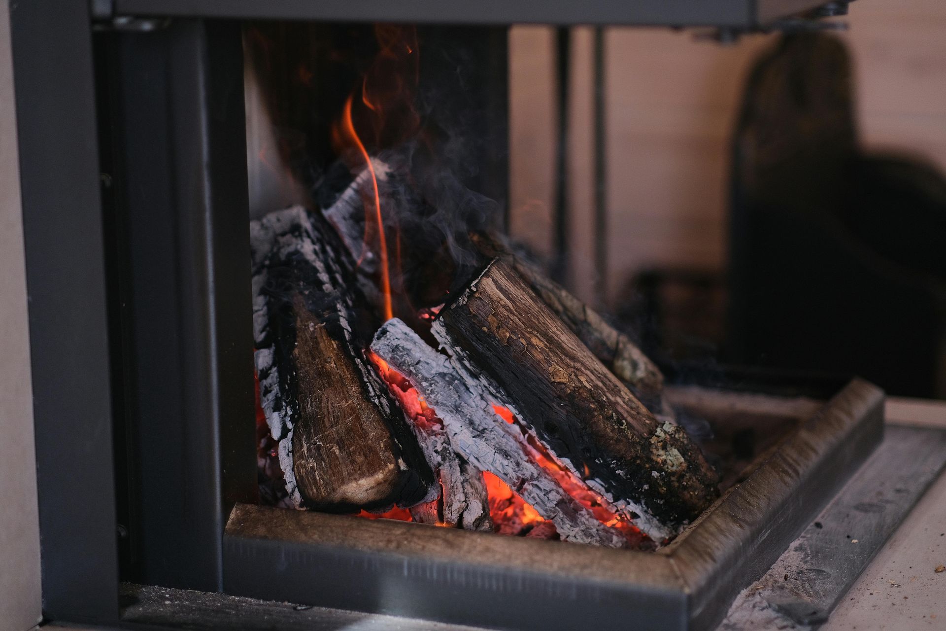 Logs burn with bright orange flames and glowing embers inside a modern black fireplace.