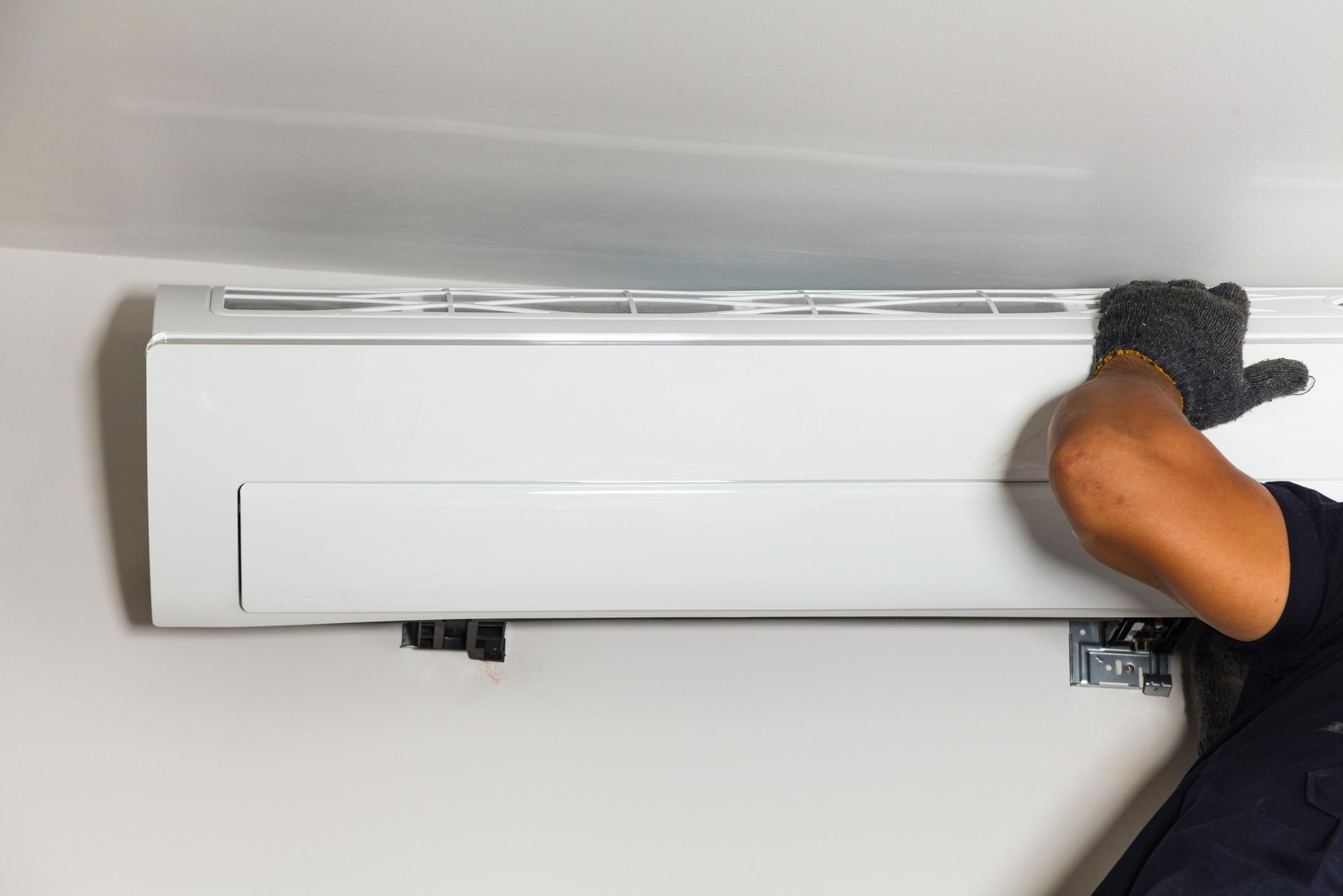 A person installing a white wall-mounted air conditioner unit.