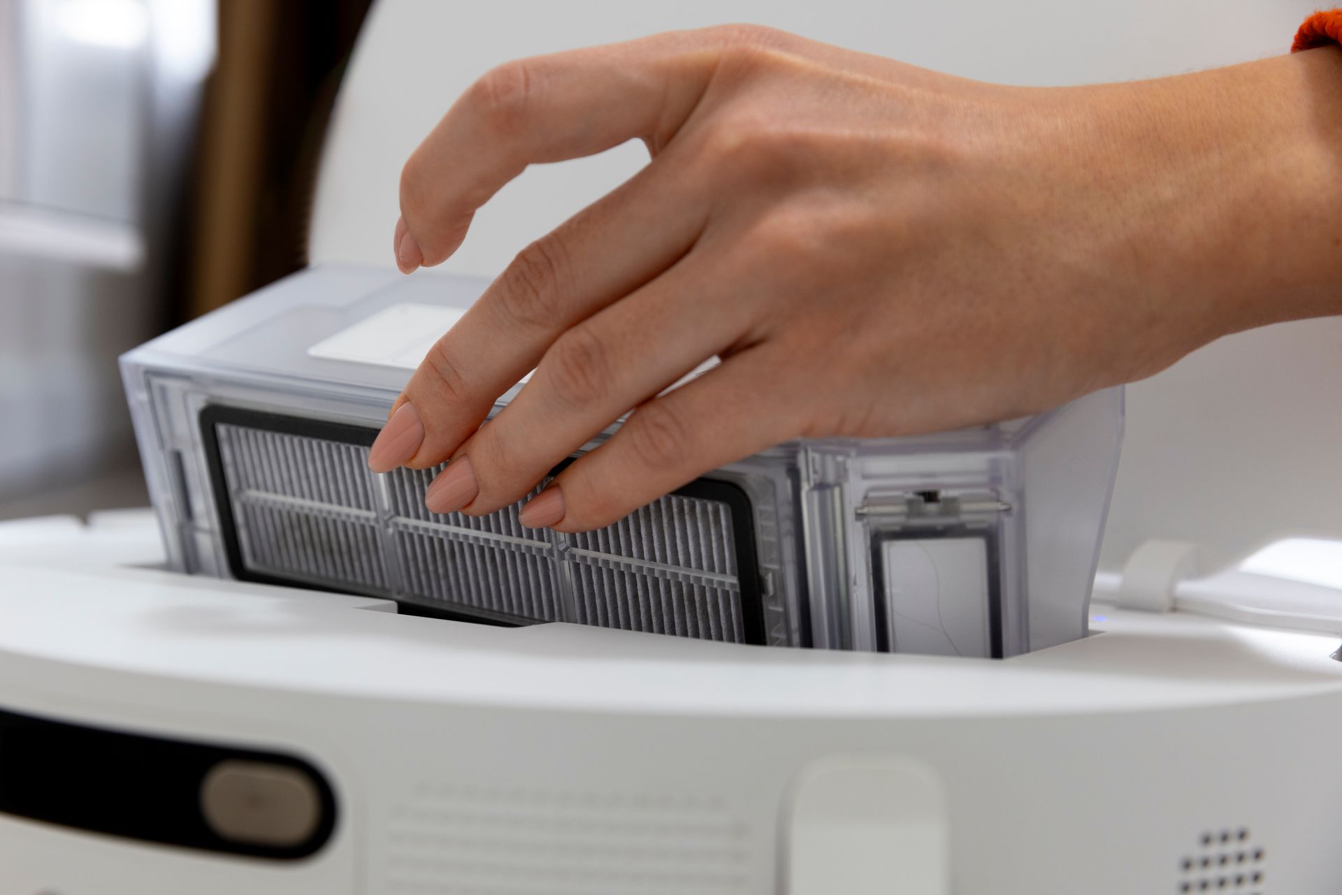 Hand removing a filter from a white robotic vacuum cleaner.