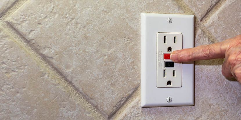 A person is pressing a button on a wall outlet.