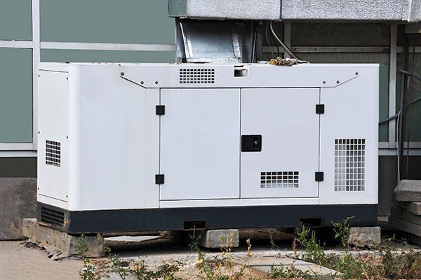 A white generator is sitting outside of a building.