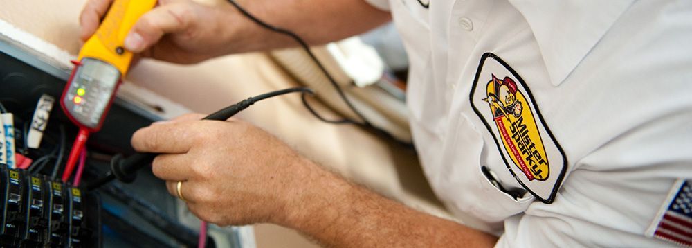 A man in a white shirt is working on an electrical box with a voltage detector.