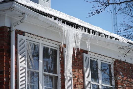 Icicles are hanging from the roof of a brick house.