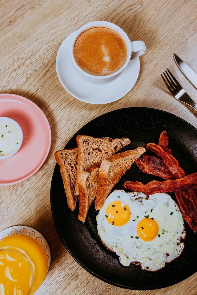Desayuno: Huevos fritos, tostadas, tocino, café, jugo de naranja y una guarnición de salsa en una mesa de madera.