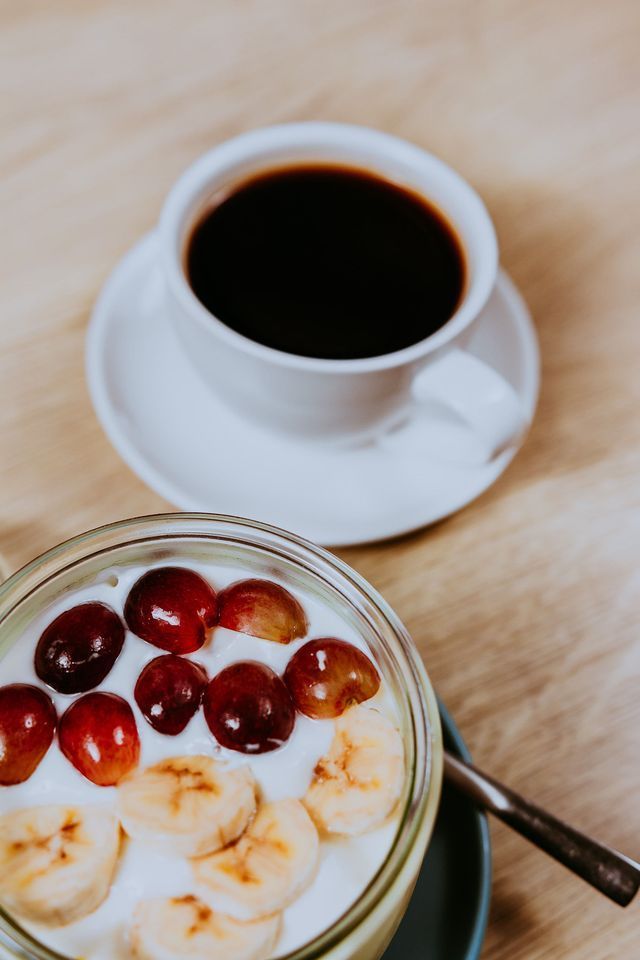 Café y yogur con fruta en una mesa de madera.
