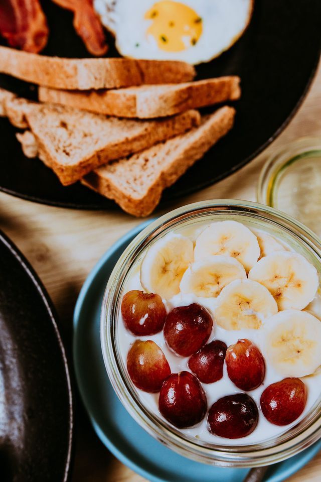 Plato de desayuno con tostadas, huevo, tocino y yogur con fruta.
