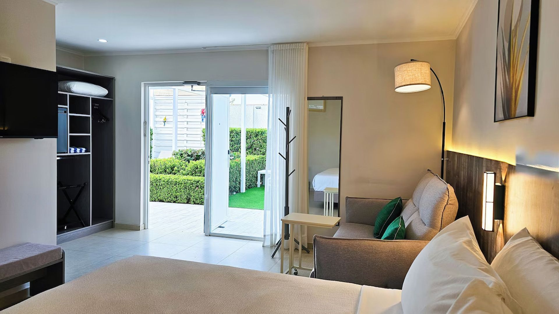 Habitación de hotel con cama, zona de estar y puertas que dan a un jardín.