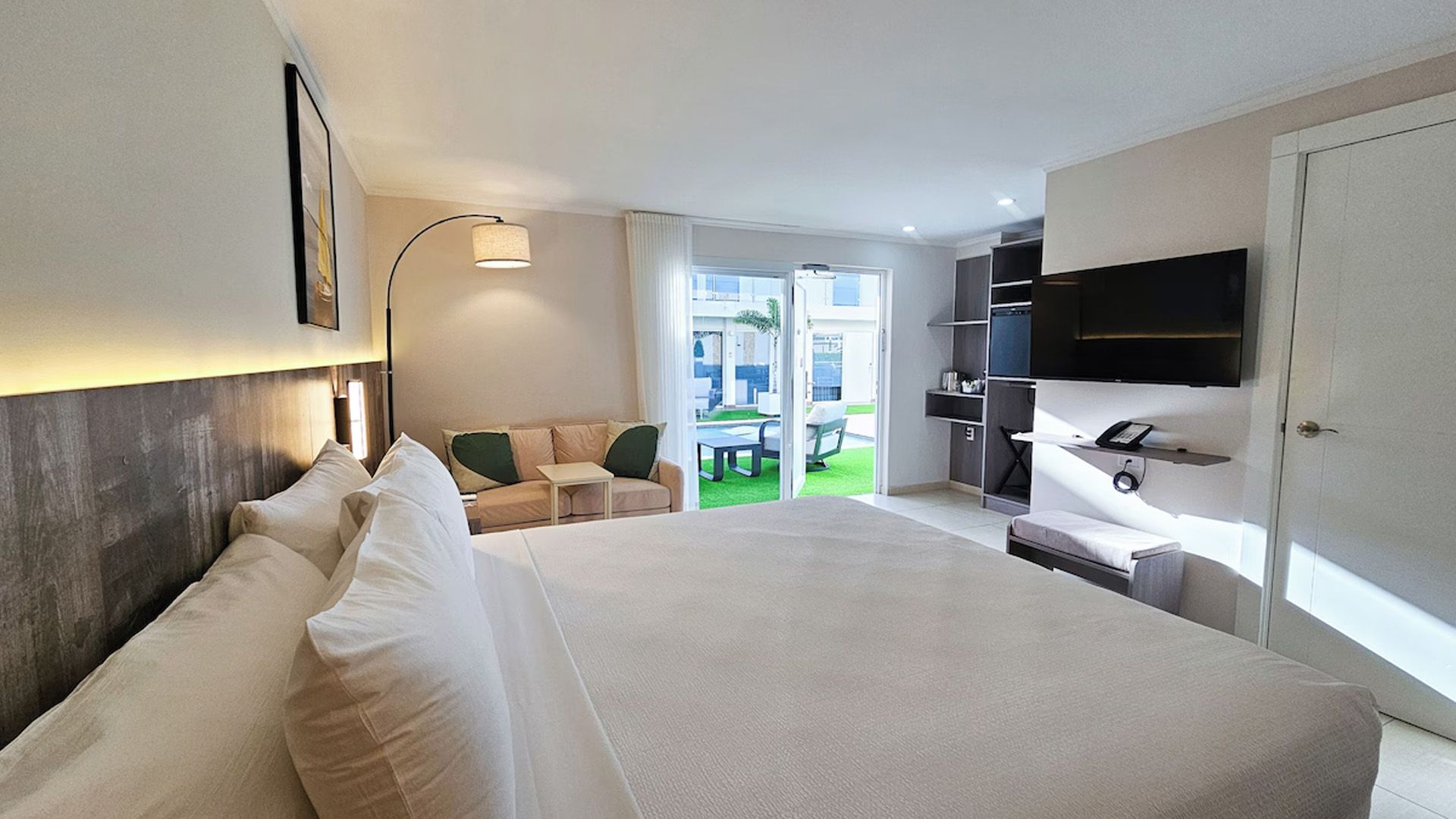 Habitación de hotel con cama, sofá, TV y vista a un patio.