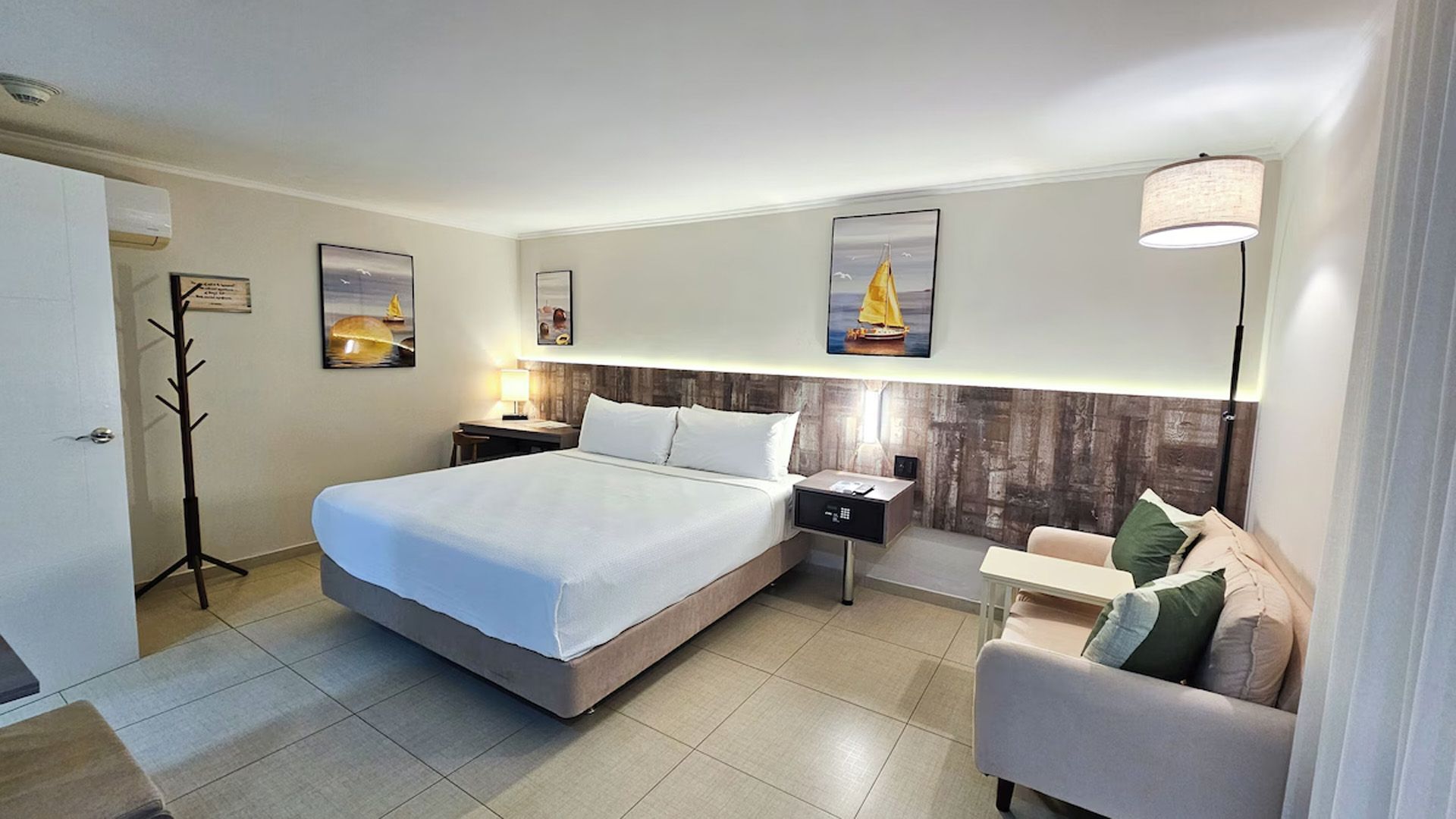 Habitación de hotel con una cama, un pequeño sofá y cuadros.