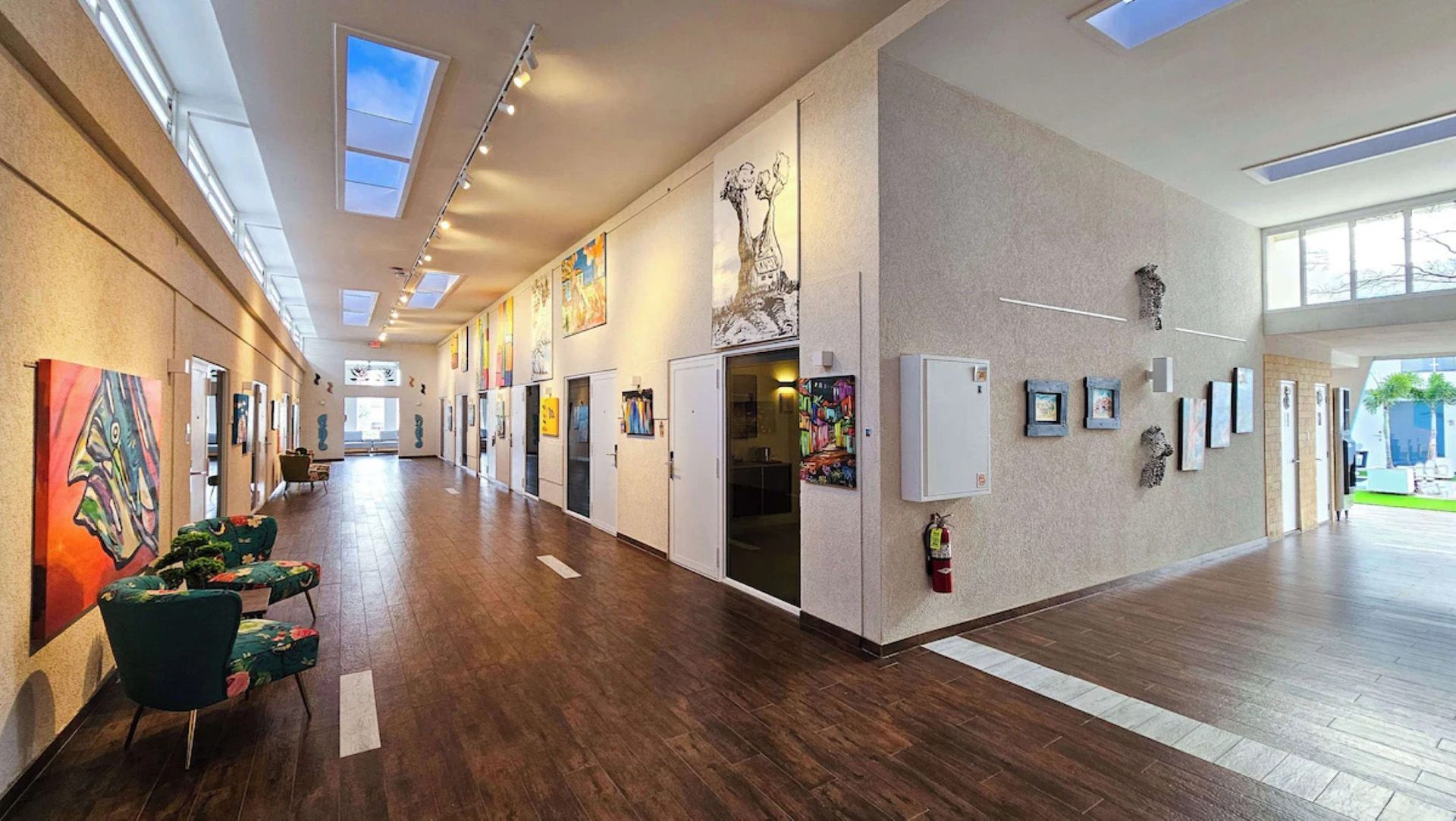 Pasillo largo en una galería de arte con pinturas, asientos y luz natural procedente de tragaluces.