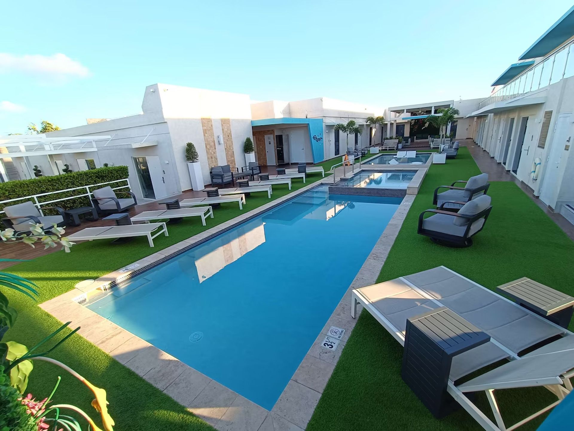 Área de piscina con camastros, agua azul y un moderno edificio blanco.