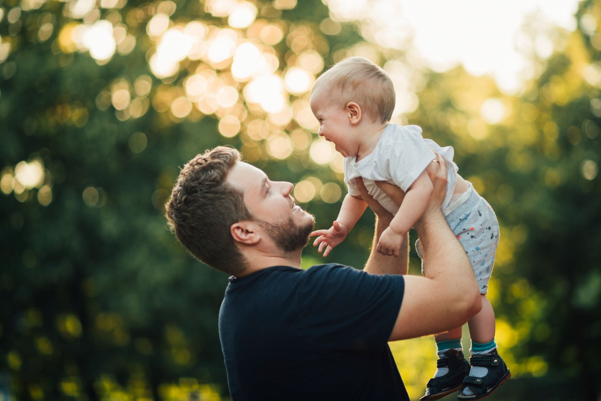 A man is holding a baby in his arms in the air.