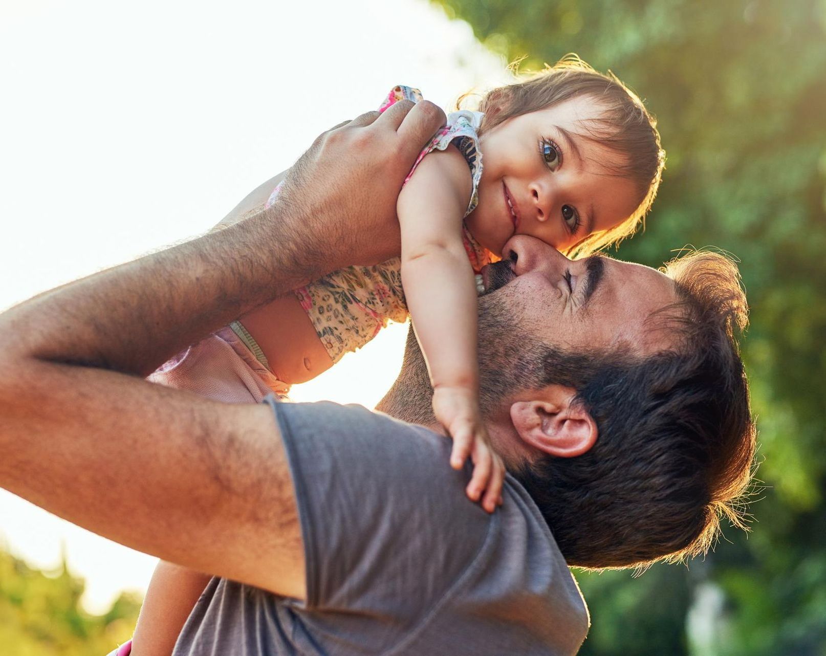 A man is holding a baby girl in his arms and kissing her on the cheek.