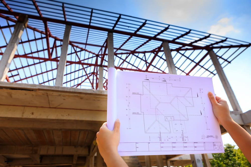 A Person Holding A Blueprint In Front Of A Building Under Construction — Burton Group In Ciccone, NT