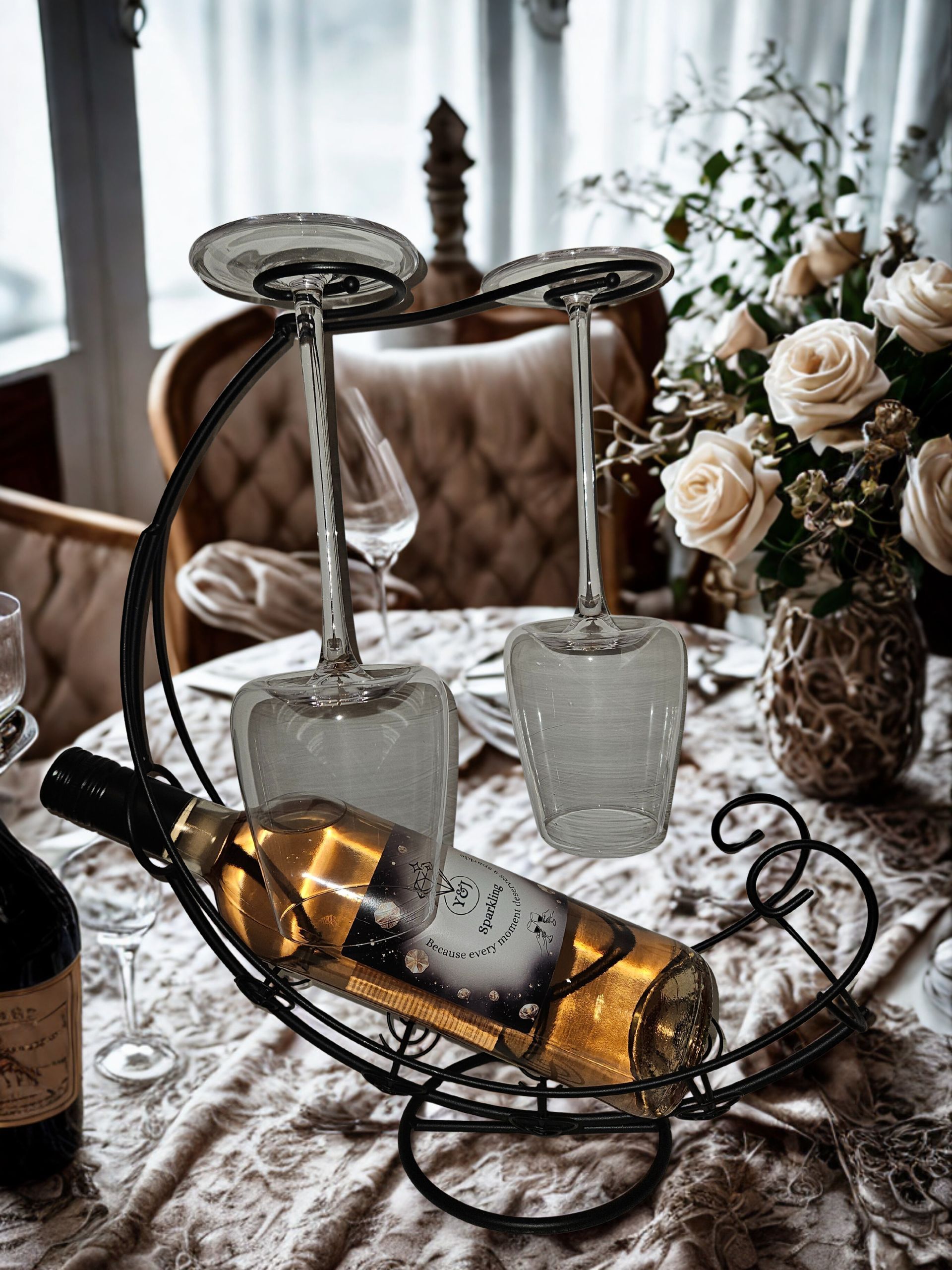 Een wijnfles en twee glazen in een decoratief metalen rekje op een eettafel met servies.