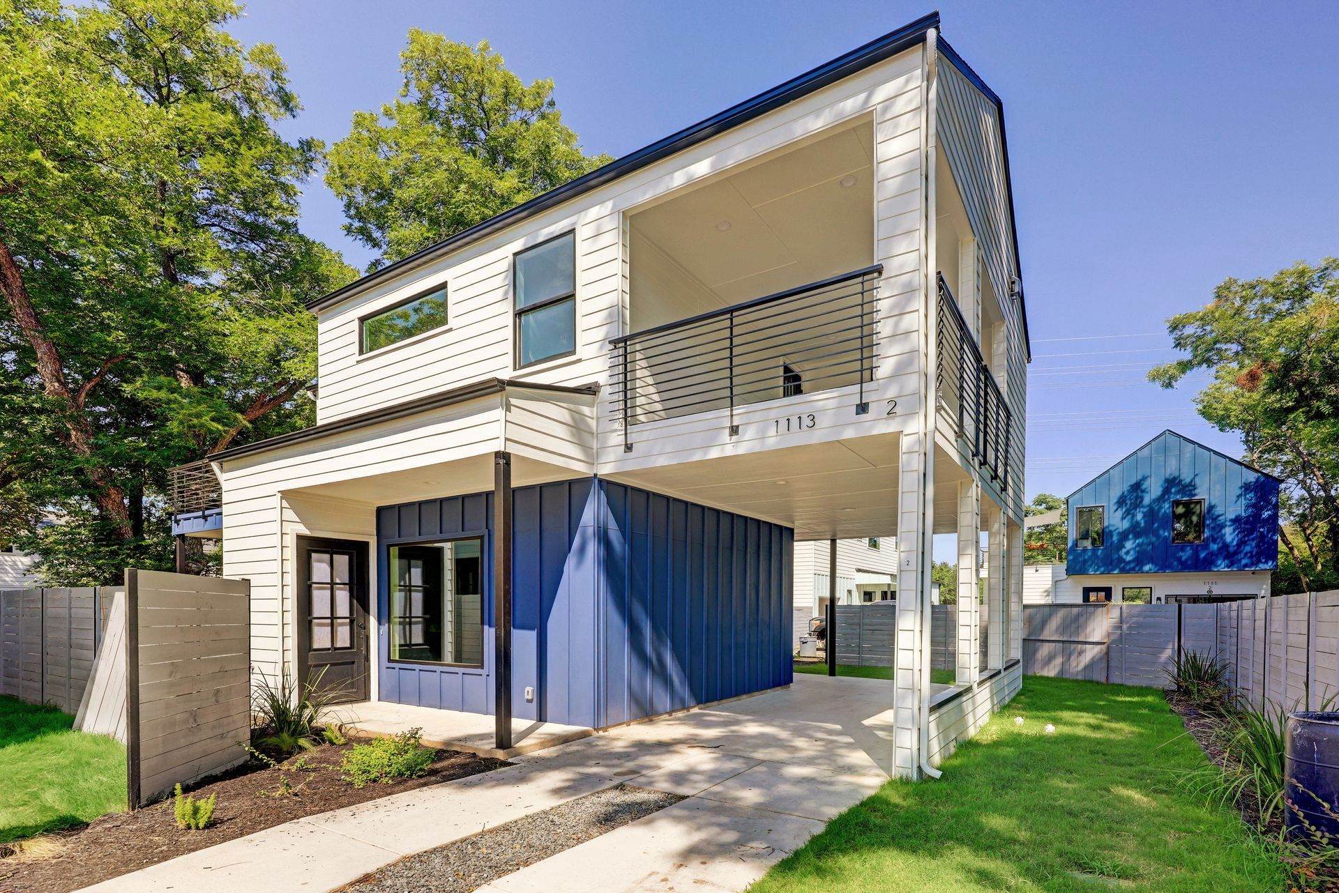 A white and blue house with a balcony and a fence in front of it.
