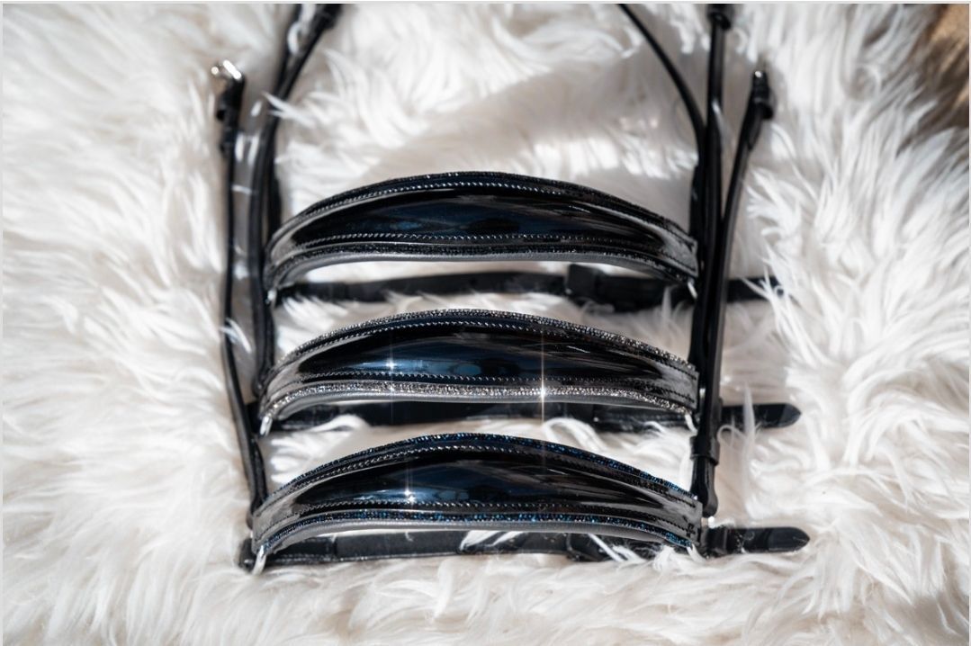 Zwart paardenhoofdstel met drie glanzende, gewatteerde frontriemen op een wit, pluizig oppervlak.