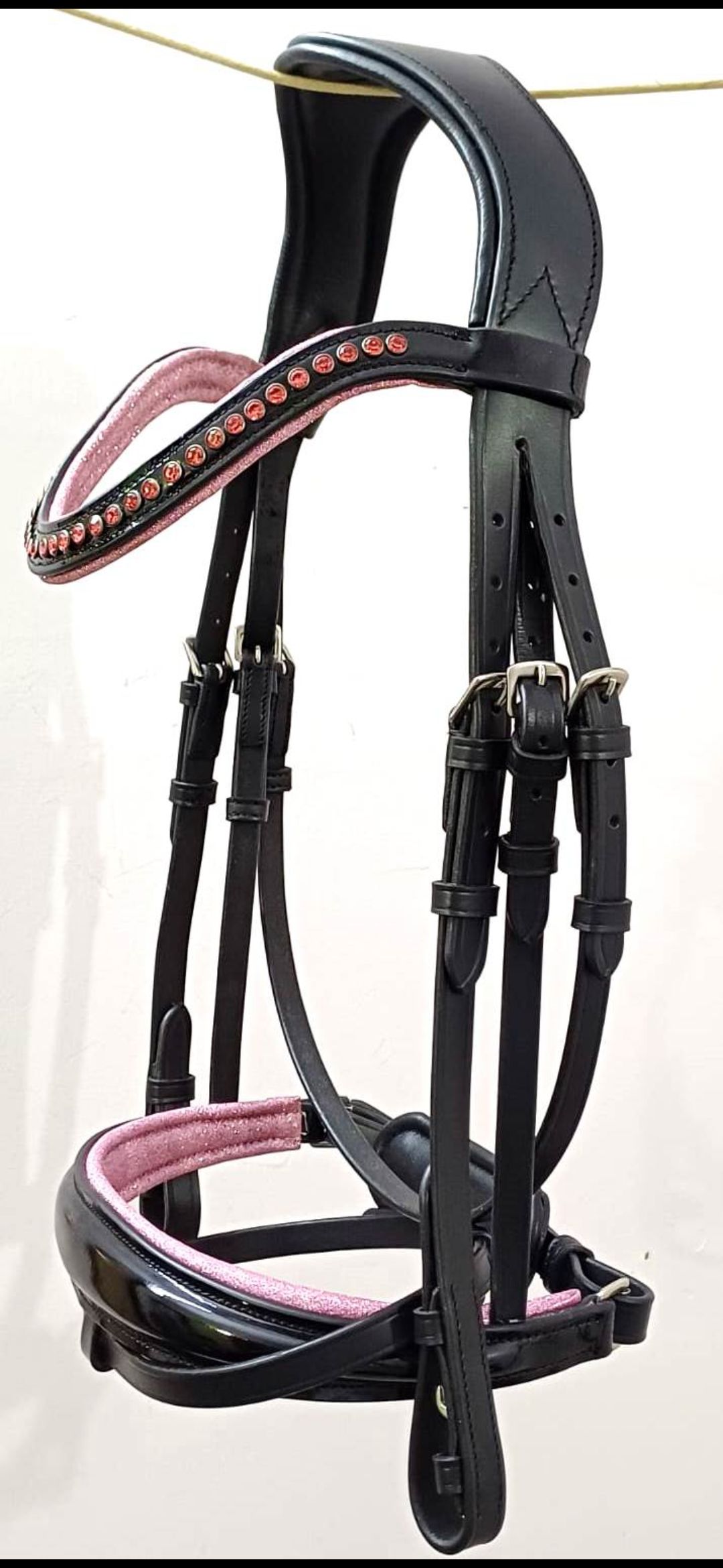 Een zwart leren paardenhoofdstel met roze vulling op de frontriem en neusriem, opgehangen tegen een effen achtergrond.