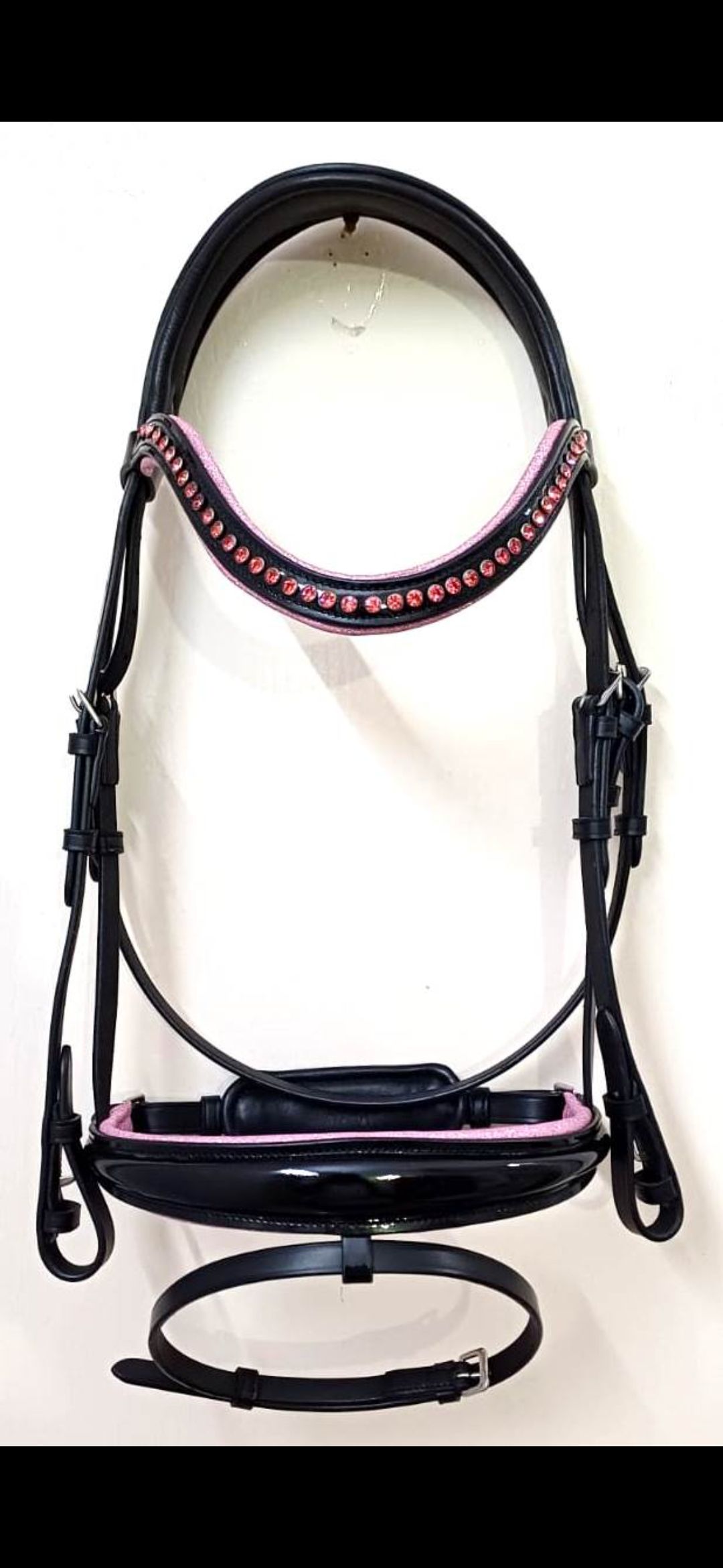 Een zwart leren paardenhoofdstel met roze vulling op de frontriem en neusriem, opgehangen tegen een effen achtergrond.