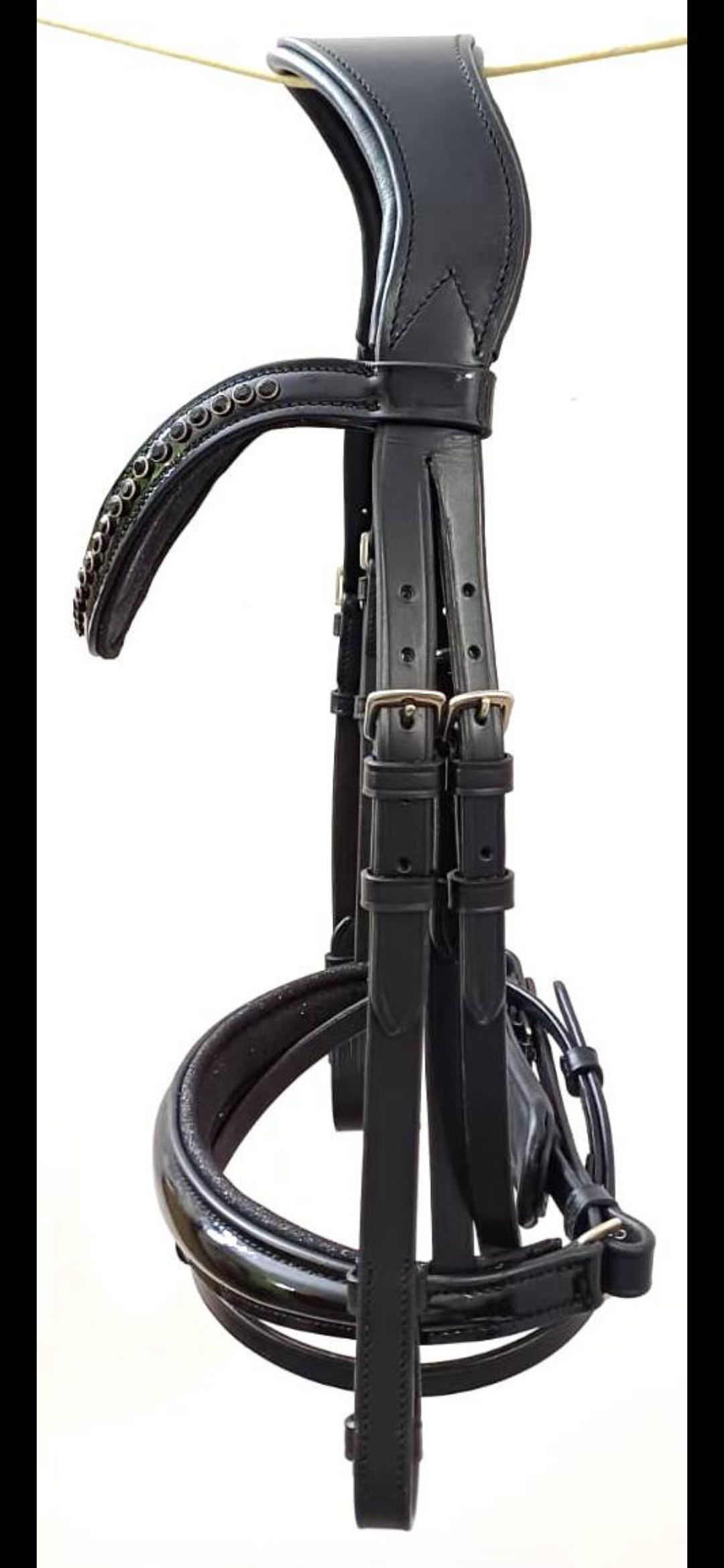 Een zwart leren paardenhoofdstel met een gewatteerd kopstuk, een frontriem met kristallen inleg en een neusriem van lakleer.