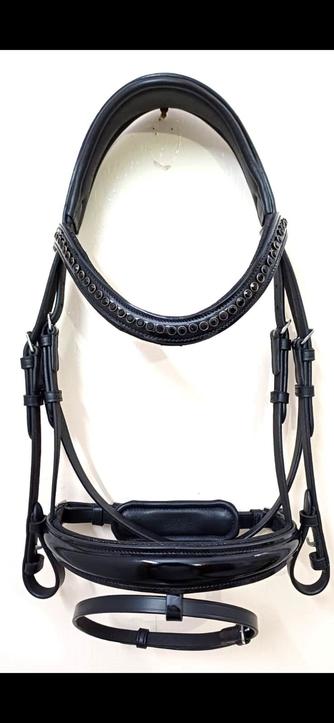 Een zwart leren paardenhoofdstel met een gewatteerd kopstuk, een frontriem met kristallen inleg en een neusriem van lakleer.