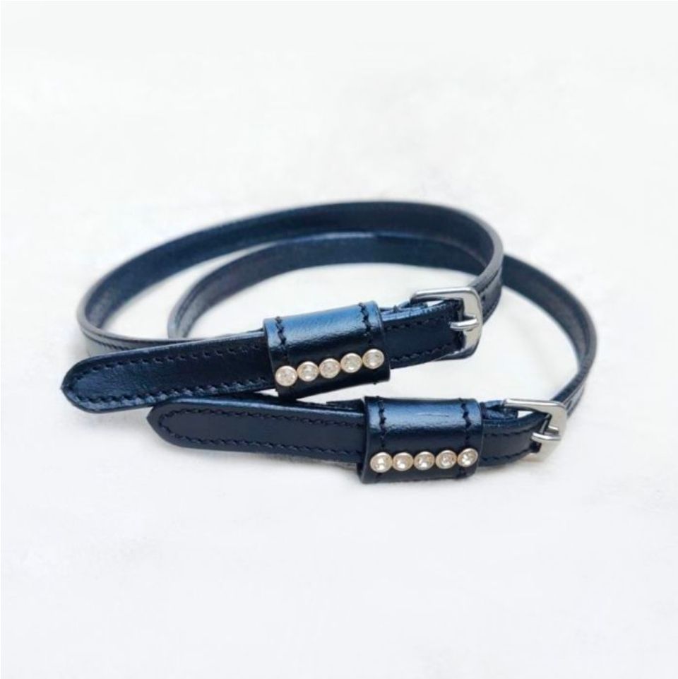Twee dunne, donkerblauwe leren bandjes met zilveren gespen en een rij van vijf decoratieve kristallen op elk lipje.