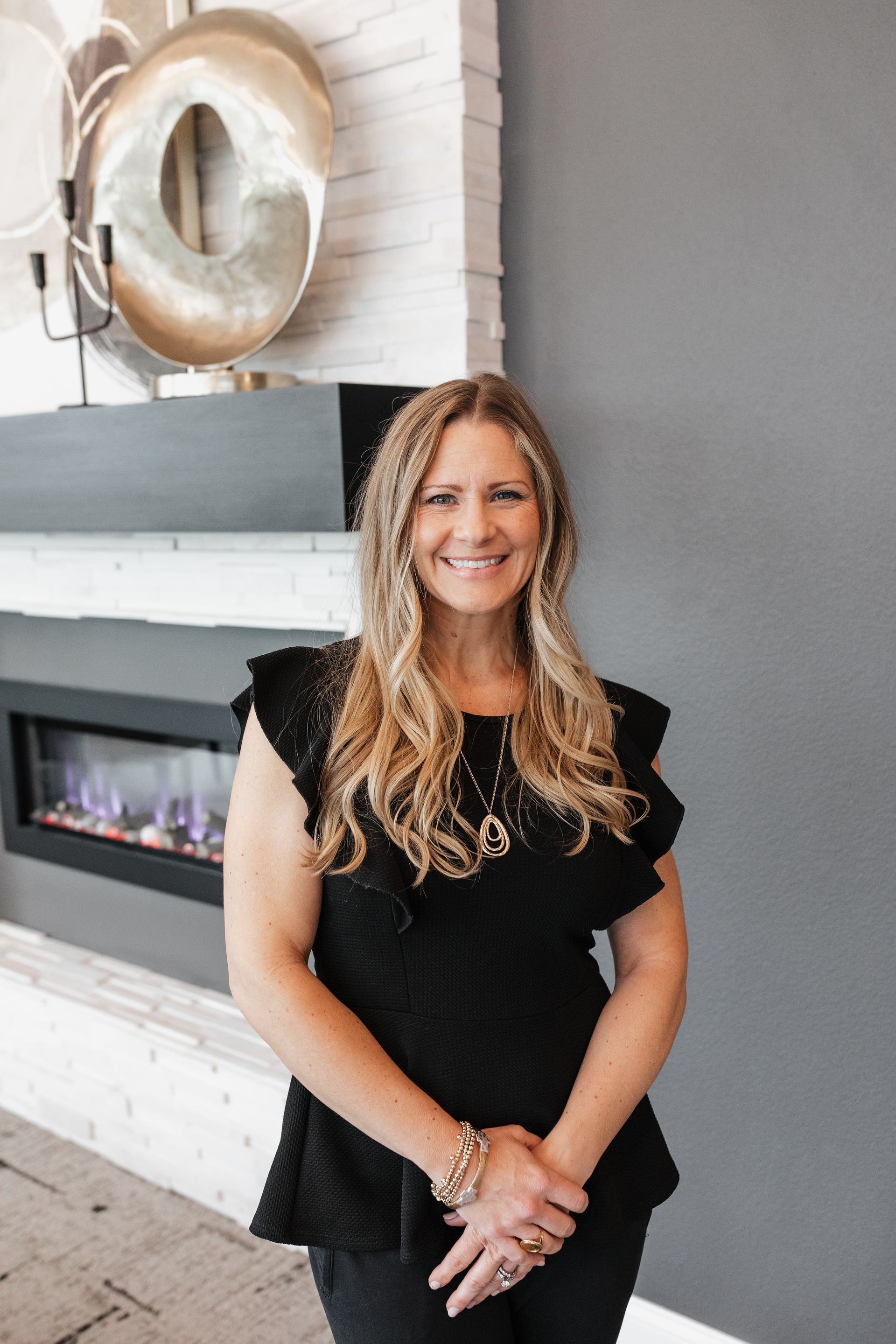 A woman in a black top is standing in front of a fireplace.