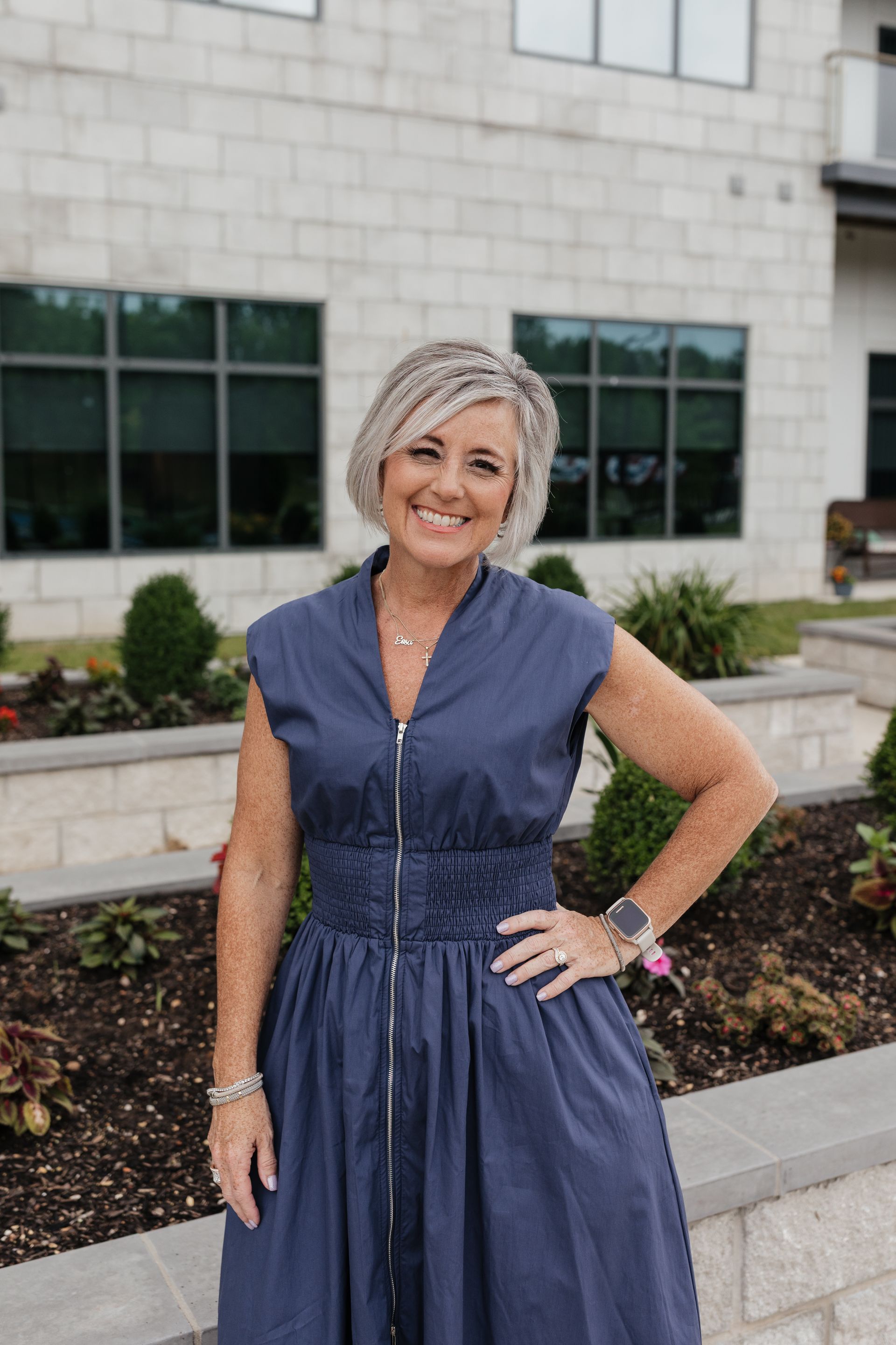 A woman in a blue dress is standing in front of a building.