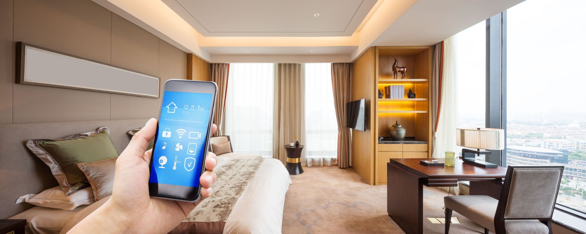 Hand holding a smartphone displaying a smart home app in a hotel room.